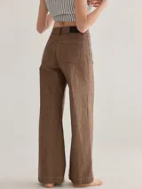 Pantalón gris de tiro medio alto, corte ancho, con bolsillos delanteros y traseros, detalles de atraques y triples costuras en color amarillo.