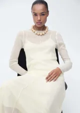 Vestido largo color crema, de corte recto y diseño semitransparente. Incluye forro interior y mangas largas.