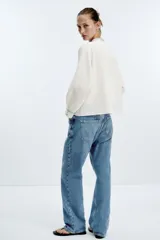 Blusa blanca de cuello redondo con cordón con borlas, escote pico y manga larga. Detalle de bordados combinados a contraste en azul.