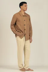 Campera color marrón claro estilo sobrecamisa confeccionada en lino premium. Cuenta con cuello clásico, cierre frontal con botones, un bolsillo de parche en el pecho y dos bolsillos de parche en la parte inferior.