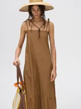 Vestido midi de denim algodón color marrón, con escote recto y tirantes finos ajustables con lazos. El corte es suelto y termina con un ruedo con semi-volado.