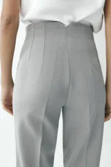 Pantalón gris de tiro alto con costuras marcadas en delantero y espalda, bolsillos delanteros de vivo y cierre frontal con cremallera, botón interior y gancho metálico.