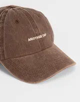 Gorra de gabardina color marrón con efecto lavado y bordado frontal con la frase "Another Cap". Ajuste trasero con hebilla metálica.