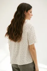 Camisa blanca con estampado de lunares negros, de corte clásico, manga corta y cuello camisero.