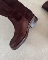 Botín corto de cuero vacuno color beige, estilo cowboy, con caña media y costuras decorativas en forma de onda en el empeine. Presenta un taco bajo y suela con pespunte visible.