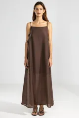 Vestido largo color marrón chocolate, con breteles finos y escote recto. Presenta lazos en los costados, forro hasta arriba de las rodillas y caída posterior más larga.