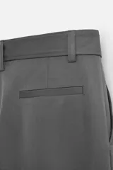 Pantalón negro de corte ancho con cinturón de tela con hebilla metálica y pliegues frontales.