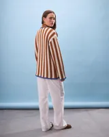 Cárdigan tejido a rayas verticales color beige y marrón, con cuello marrón y detalles en azul. Cierre frontal con nudos y bolsillos delanteros.