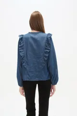 Blusa blanca de calce holgado con cuello en V y lazo frontal. Presenta detalles de volados en el pecho y cuello, y mangas largas con puños elásticos.