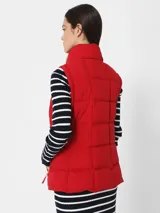 Chaleco rojo acolchado con cuello alto, cierre frontal con cremallera dorada y bolsillos laterales con cremallera dorada.