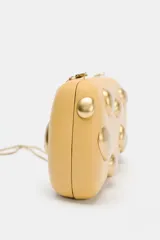 Bolso de mano tipo clutch color beige con apliques metálicos dorados. Incluye cadena metálica extraíble para usar como bandolera.