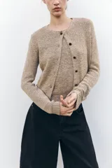 Chaqueta color beige de punto con cuello redondo, manga larga, rib en los bordes y cierre frontal con botones negros.