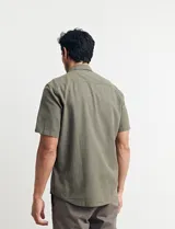 Camisa sport de manga corta color verde oliva, línea premium, con cuello clásico, cierre frontal con botones de coco y bolsillo de parche en el pecho. Confeccionada en lino y algodón.