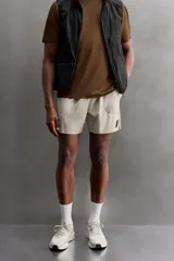 Shorts deportivos marrones de tejido técnico ligero y elástico con diferentes estructuras. Tiene forro interior, cintura elástica ajustable con cordón, bolsillos frontales, bolsillo trasero con cierre, aberturas laterales y logo estampado en la pierna.