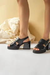 Sandalias negras de charol con plataforma y tacón cuadrado. Presentan tiras anchas cruzadas en el empeine y correa ajustable en el tobillo.