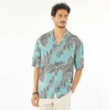 Camisa celeste con estampado de hojas de palmera en tonos negro y blanco, de corte recto, con cuello cubano y mangas cortas con dobladillo.