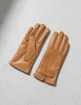 Guantes de cuero sintético color camel, con forro interior de terciopelo. Presentan un diseño clásico con costuras decorativas en el dorso y una tira ajustable con botón a presión en la muñeca.