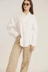 Camisa blanca de manga larga, corte holgado, con cuello camisero y detalles de bordados perforados (calado) verticales en el frente.