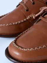 Mocasín de cuero color marrón claro, con cordones y detalle de costuras en la puntera.