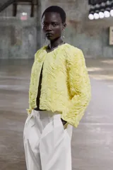 Chaqueta corta color amarillo pastel con textura de volantes, cuello redondo, manga larga y cierre frontal con botón a presión oculto.