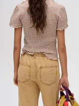 Mono largo de jean celeste con corte holgado, cintura elastizada con cordón ajustable, sin mangas, cuello camisero y cierre frontal con botones. Presenta bordados de motivos playeros en el pecho.