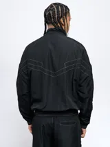 Campera deportiva Umbro de nylon con diseño color block en blanco, azul y rojo. Tiene cuello alto, cierre frontal con cremallera y bolsillos laterales. Logo de Umbro bordado en el pecho.