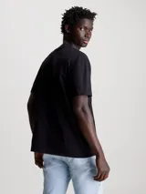 Remera negra de algodón con cuello redondo y mangas cortas. Estampado frontal con el logo de Calvin Klein Jeans en letras blancas con detalles fotográficos en colores celeste, rosa y gris.
