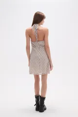 Vestido corto de poliéster, ajustado al cuerpo, con cuello halter y escote en V. Presenta un estampado de cuadros en tonos beige y negro/gris oscuro.