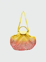 Bolso tipo tote de red color amarillo con degradé naranja en la parte inferior. Tiene solapa de cuero con botón a presión y asas cortas para llevar al hombro.