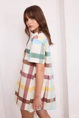 Vestido corto de algodón a cuadros color crema, verde y borgoña, con cuello redondo y mangas cortas. Presenta tablas en la parte delantera y trasera.