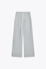 Pantalón de tiro medio color celeste confeccionado en hilatura con mezcla de lyocell. Tiene bolsillos laterales, pinzas en el delantero y pierna ancha. Cierre frontal con cremallera, botón y ganchos metálicos.