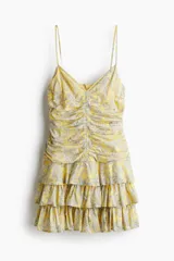 Vestido corto amarillo con estampado paisley, escote en V, breteles finos ajustables y falda escalonada con volados. Presenta un cierre oculto en la espalda y forro interior.