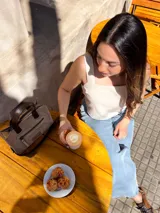 Cartera tipo tote de cuero color beige, con doble asa corta marrón y cierre superior con cremallera. Tiene un bolsillo frontal con cremallera y forro interior de tela con un bolsillo.