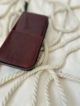 Billetera grande de cuero color borgoña, con cierre metálico y logo de la marca grabado. Incluye moneda colgante plateada con el logo de la marca.