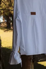 Camisa blanca de lino con cuello alto con volados y mangas largas.