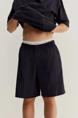 Conjunto de pijama corto de dos piezas. Remera negra de punto de algodón liviano con cuello redondo ribeteado acanalado, hombros caídos y bajo recto. Short negro en popelina de algodón con elástico revestido en la cintura, cierre de botón, bolsillos laterales y un bolsillo parche atrás.