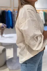 Camisa color crudo de manga larga con puños elásticos, cierre frontal con botones y bordados perforados combinados a tono en la parte delantera y trasera.