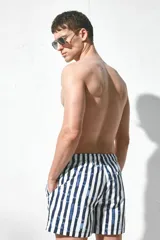 Short de baño blanco con rayas verticales azules, cintura elástica con cordón ajustable, bolsillos laterales y bolsillo trasero con cierre autoadherente. Cuenta con suspensor interior de malla suave.