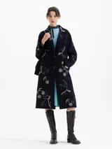 Tapado largo de paño color azul marino con bordados de piedras color cristal en forma de cerezas y pájaros. Posee cuello de solapa, cierre frontal con botones y bolsillos laterales.