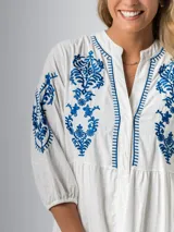 Vestido corto blanco de algodón italiano con bordado azul, mangas tres cuartos y botones frontales.