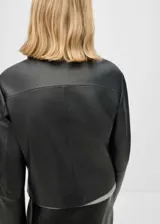 Chaqueta corta de cuero ovino color negro, con cuello camisero, cierre frontal con botones y dos bolsillos de solapa.
