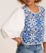 Blusa con cuerpo de tejido de ganchillo (crochet) bicolor azul y blanco con diseño floral, mangas largas abullonadas de tejido liso blanco y cuello redondo.