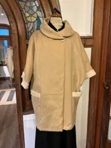 Chaquetón beige de paño con cuello alto y cierre con botón. Presenta detalle de tela marfil en puños y bordes de los bolsillos.