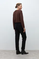 Pantalón negro de vestir, corte recto y tiro alto, con pliegues frontales y puños doblados. Se complementa con un cinturón fino negro con hebilla metálica en forma de símbolo.