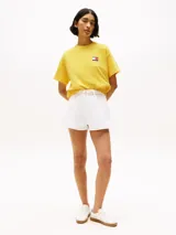 Remera amarilla de algodón con corte amplio, cuello redondo y hombros caídos. Presenta un logo pequeño de Tommy Hilfiger en el pecho, un logo en la manga y un logo grande en la espalda. Pertenece a la colección Hilfiger Sailing.
