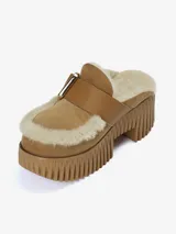 Zueco de plataforma alta confeccionado en cuero vacuno color tostado con forro de pelo de oveja. Presenta una correa con hebilla metálica ajustable en el empeine y suela de goma con diseño acanalado.