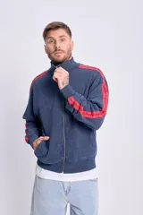 Campera deportiva con cierre frontal, cuello alto y puños y cintura acanalados. Color azul marino con efecto desgastado y dos franjas rojas a lo largo de las mangas. Presenta un pequeño logo bordado en el pecho.