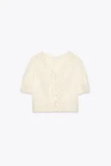 Blusa color crudo de cuello redondo y manga corta con puños. Presenta bordados a tono y cierre trasero con botones forrados.