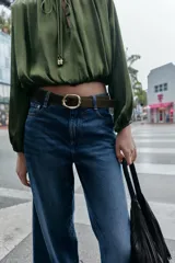 Jeans de tiro alto con pernera ancha y corte cropped. Presenta diseño de cinco bolsillos, cierre frontal con cremallera y botón, e incluye un cinturón a juego.