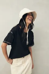 Remera blanca de algodón liviano, de manga corta y cuello redondo. Presenta costuras a contratono visibles en hombros y mangas.